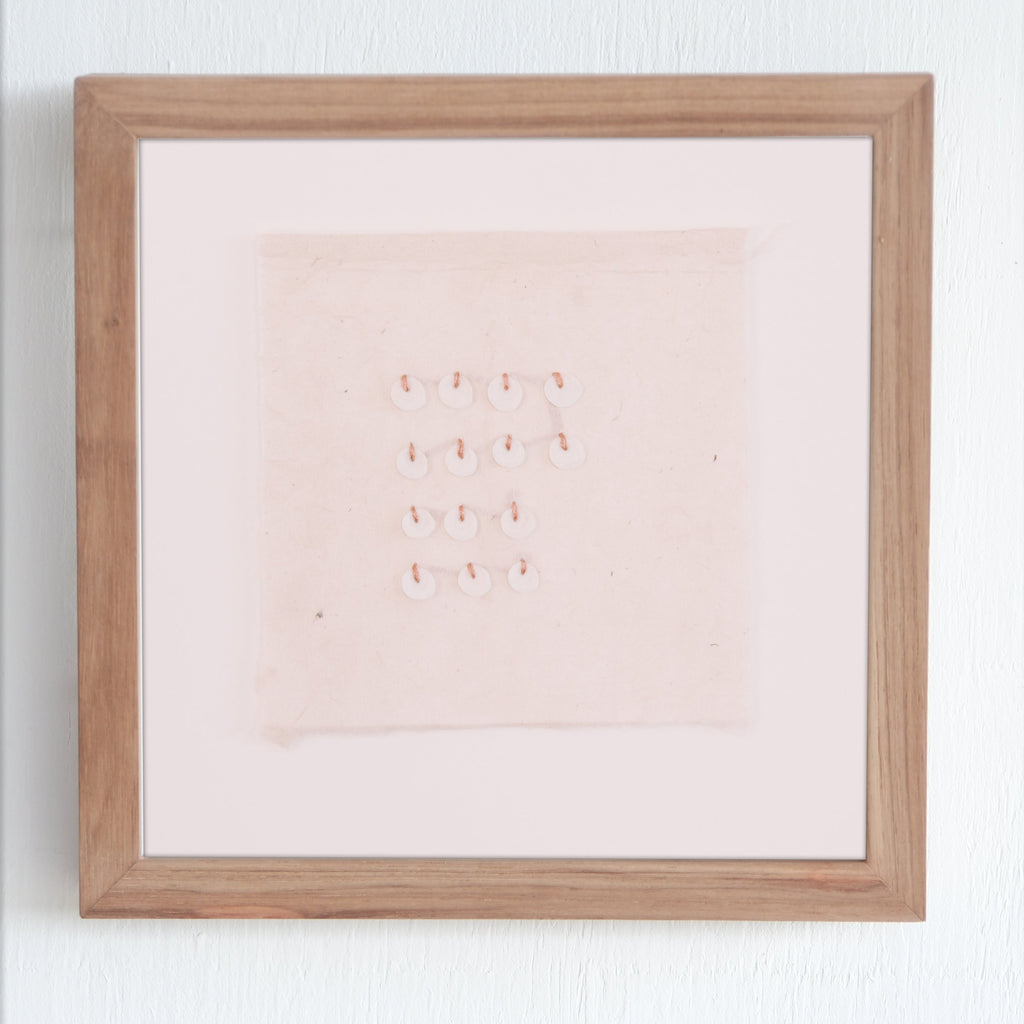 Framed artwork with hand stitching and shell on a white wall