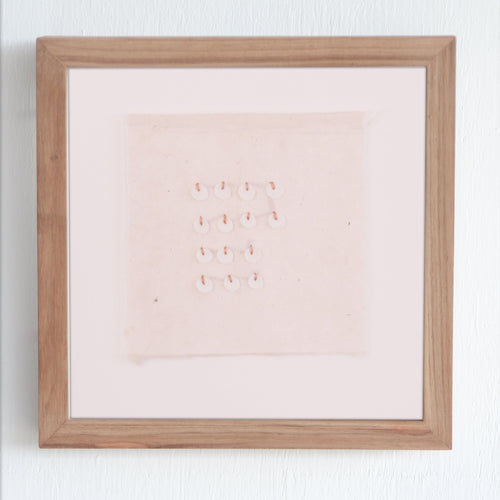 Framed artwork with hand stitching and shell on a white wall