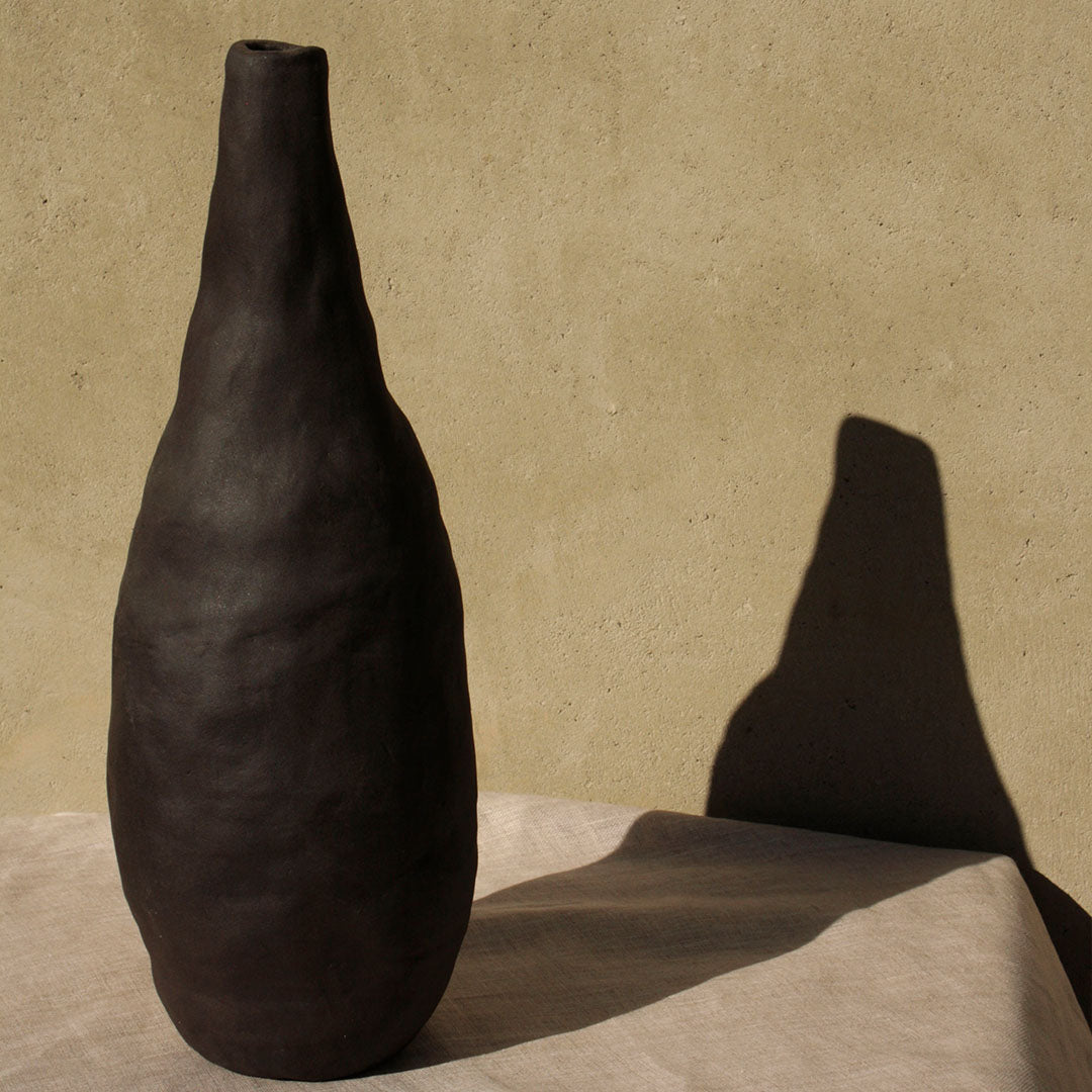 hand made ceramic vessel called Jupiter by The Adorned in black clay casting a shadow on the wall