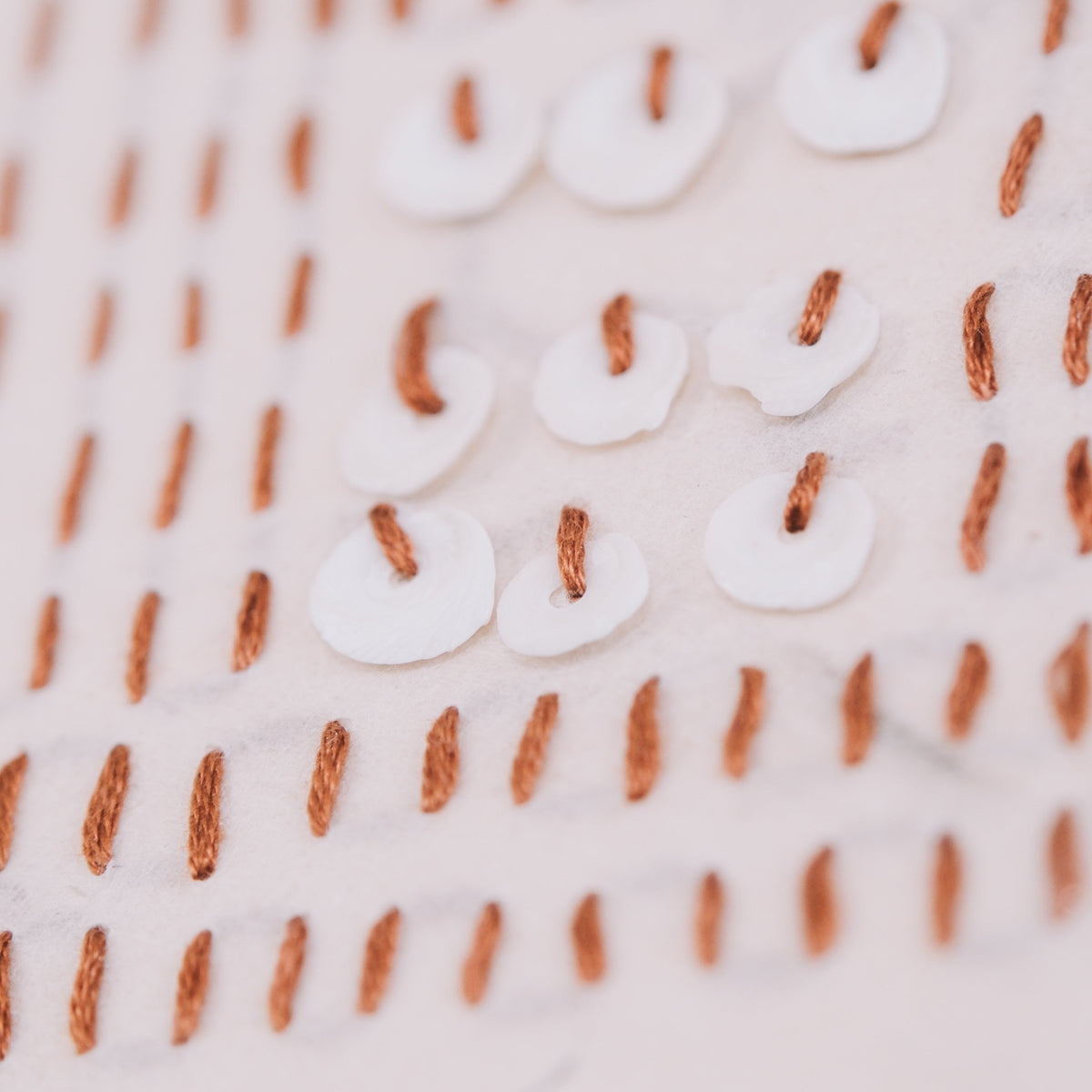 Close-up of a textured of an art work with white shells and naturally dyed thread on a nepalese paper